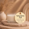 Minty Citrus Zing wickless soy candle in a clear glass vessel displayed on a textured stone pedestal with warm neutral décor and natural pampas grass accents.